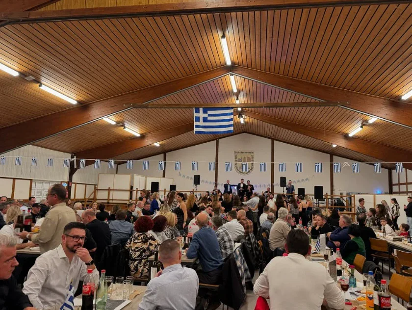 Voller Festsaal mit griechischen Fähnchen und langen Tischen